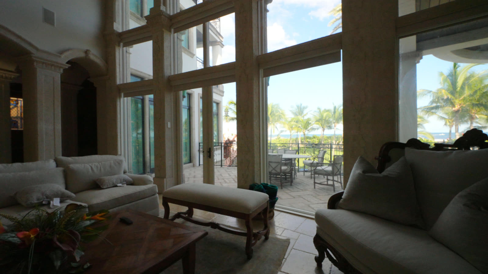 Arched window wall over the terrace with the SheerWeave Sand blackout shades raised, palms and ocean beyond