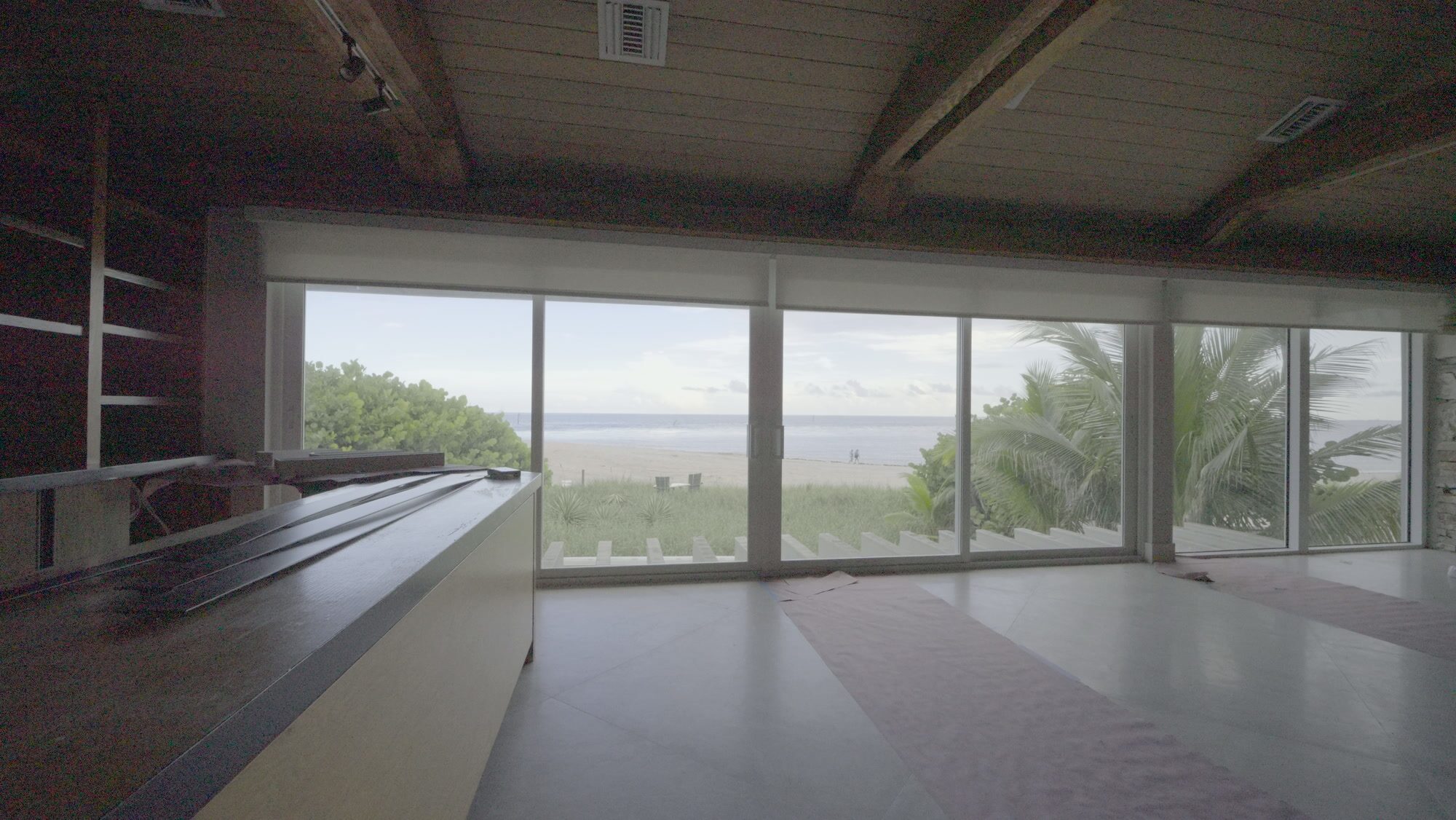 Great room with the stacked-stone fireplace wall, wood plank ceiling and shades raised to the beach view
