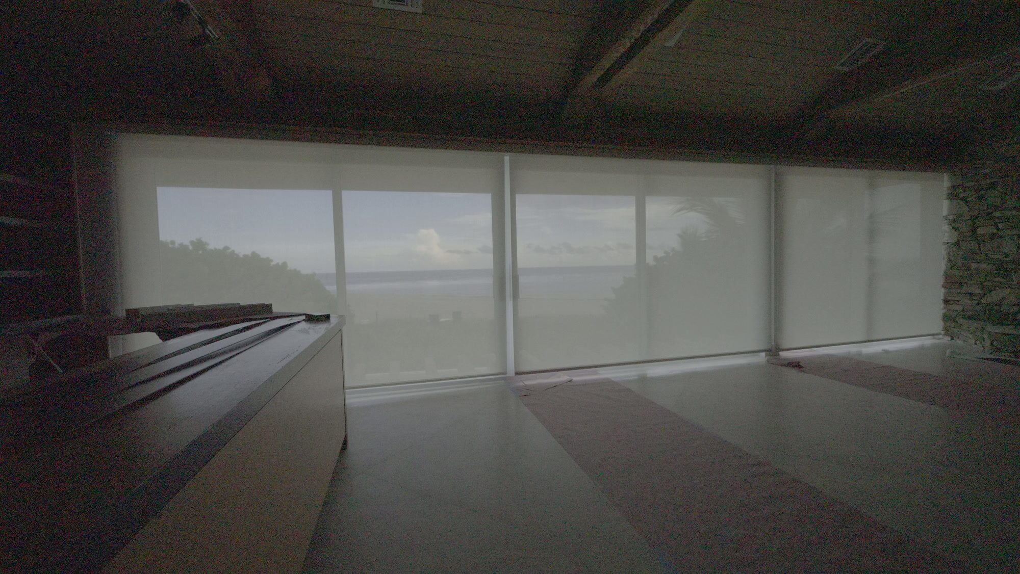 Great room with the SheerWeave 4000 Eco 5% Alabaster solar screens fully lowered, the dune and ocean still visible through the fabric