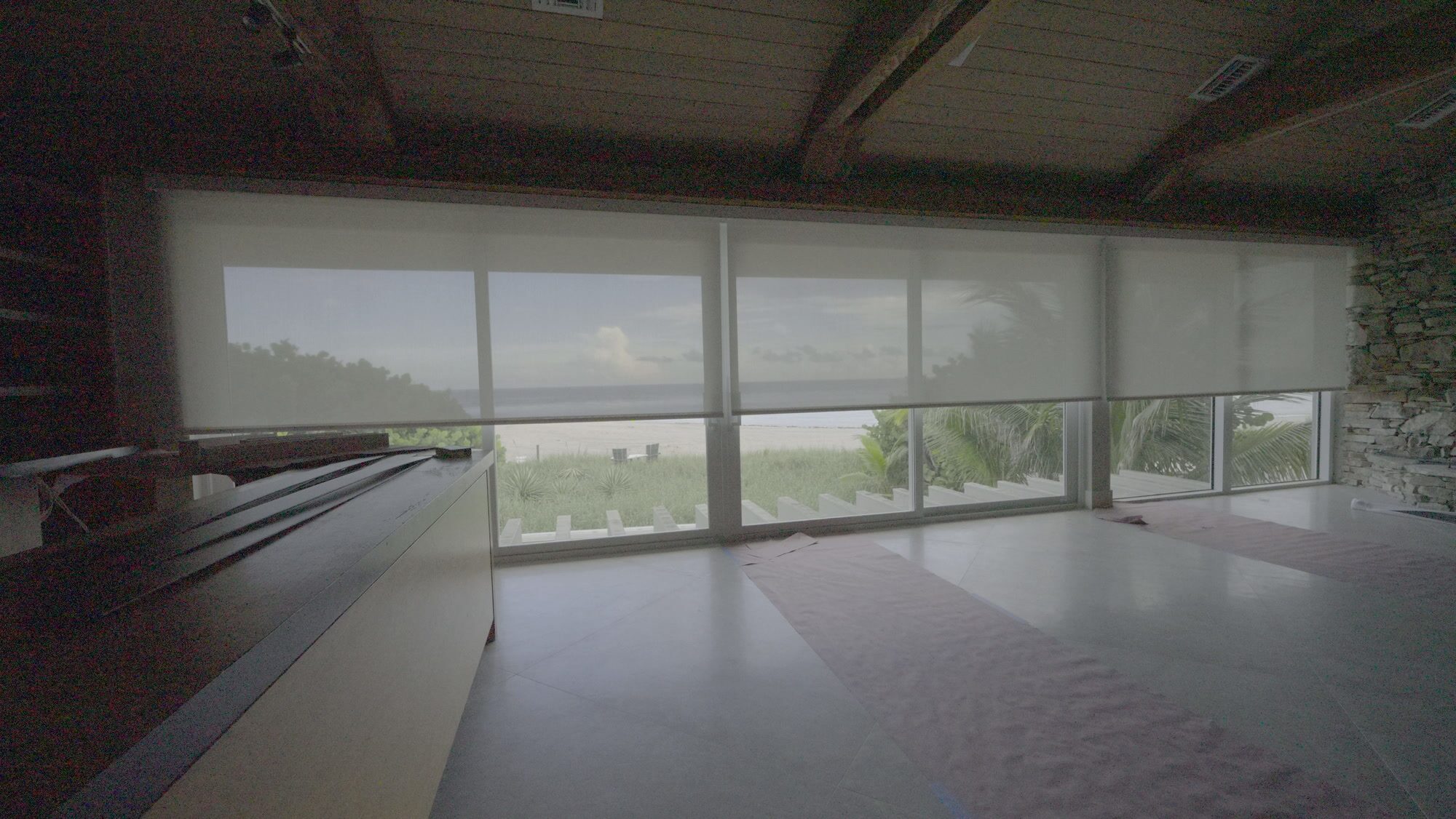 Five Somfy Sonesse 30 Zigbee roller shades lowering together across the great room sliders facing the beach in Pompano Beach