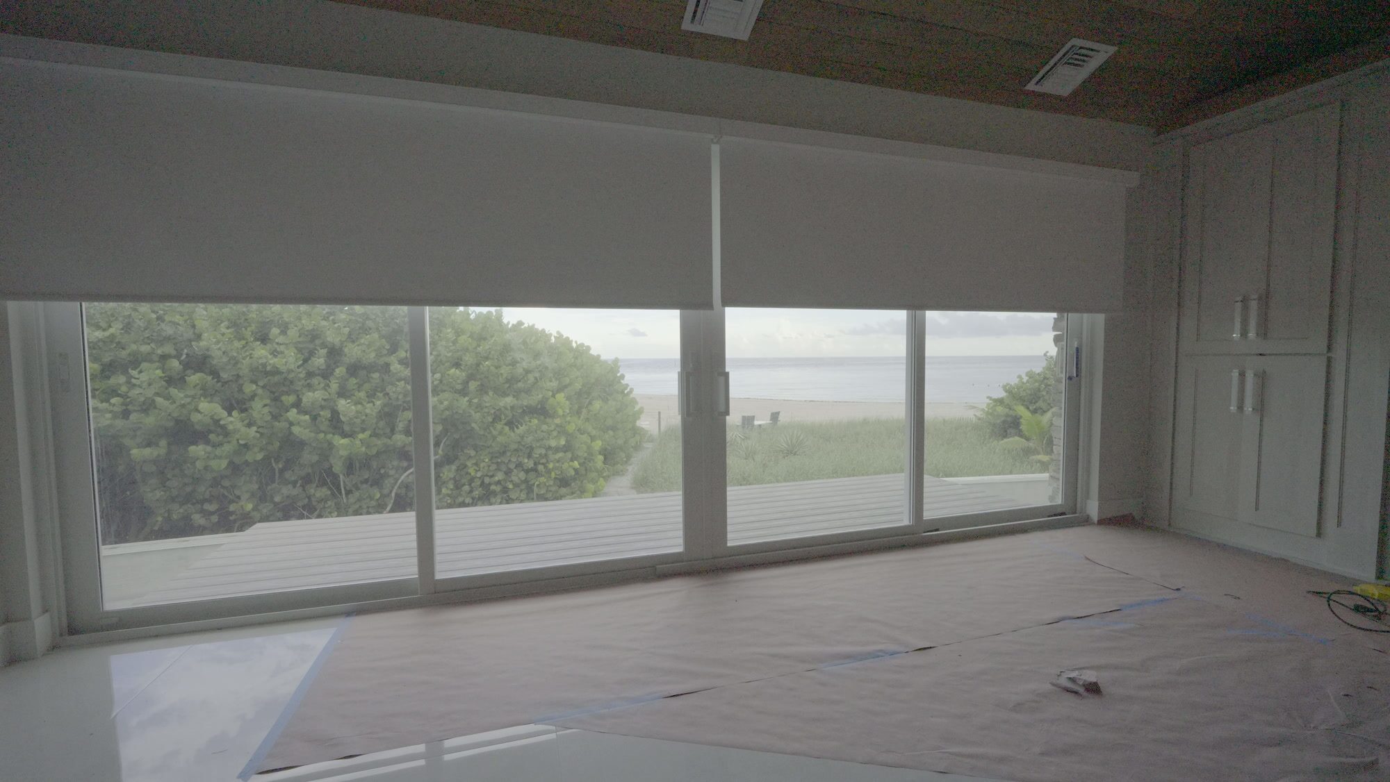 Primary suite bedroom with the SheerWeave 7200R Swan blackout shade raised, sliding glass open to the dune and the beach