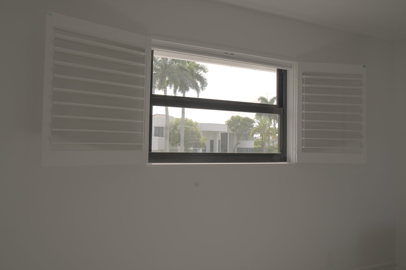 Guest house window with the shutter panels swung open and palm trees outside