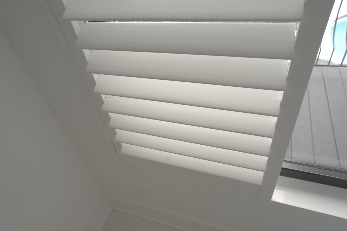 Close-up of lacquered basswood shutter louvers with no visible tilt rod on a high guest house window