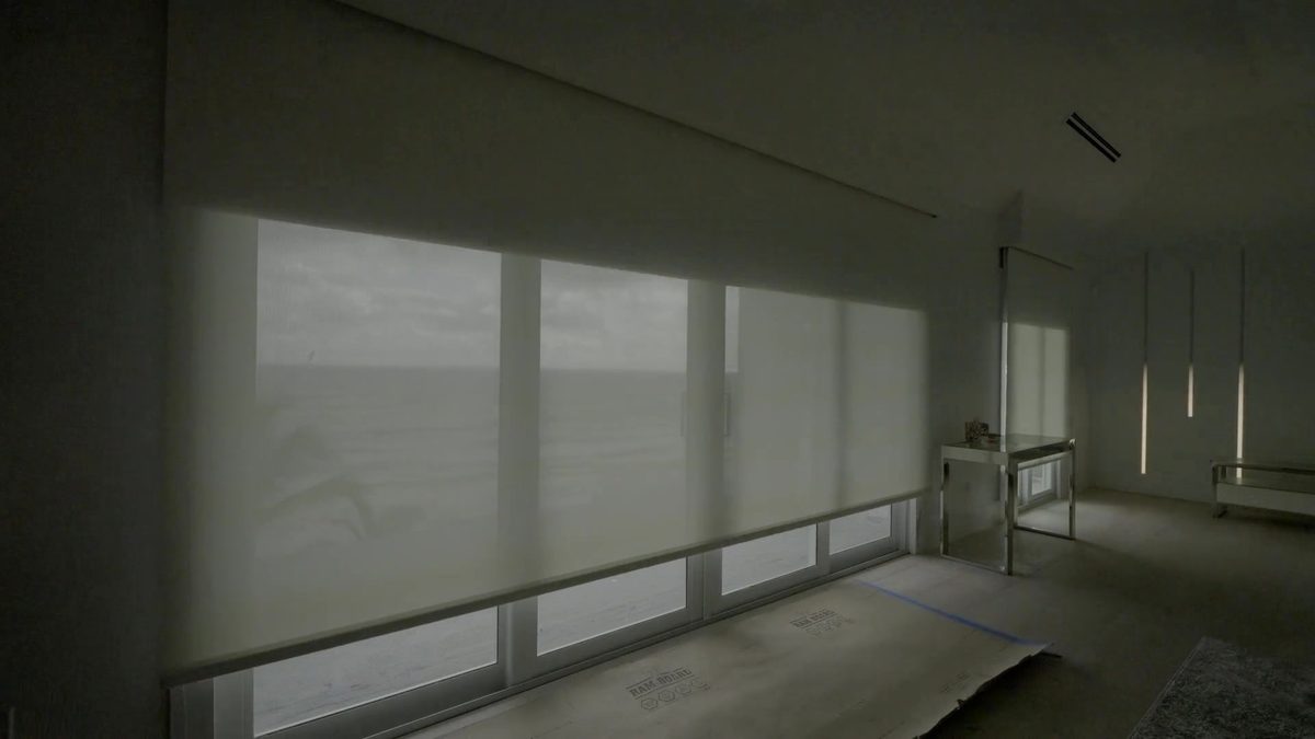 A wall of glass with the solar screen layer of a dual shade lowered, daylight still in the room