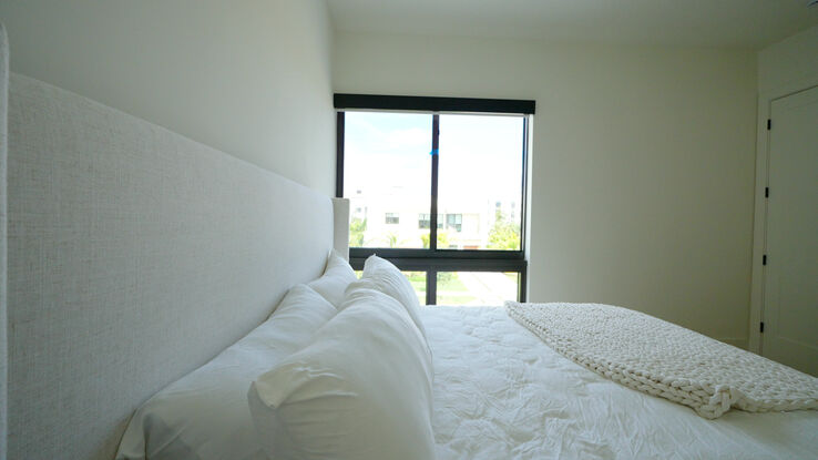 Guest bedroom with a Lutron Triathlon roller shade in Aura 5% Parchment raised over the bed