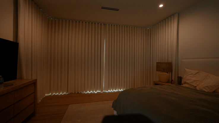 Master bedroom fully dark with the blackout drapery closed on both bent tracks