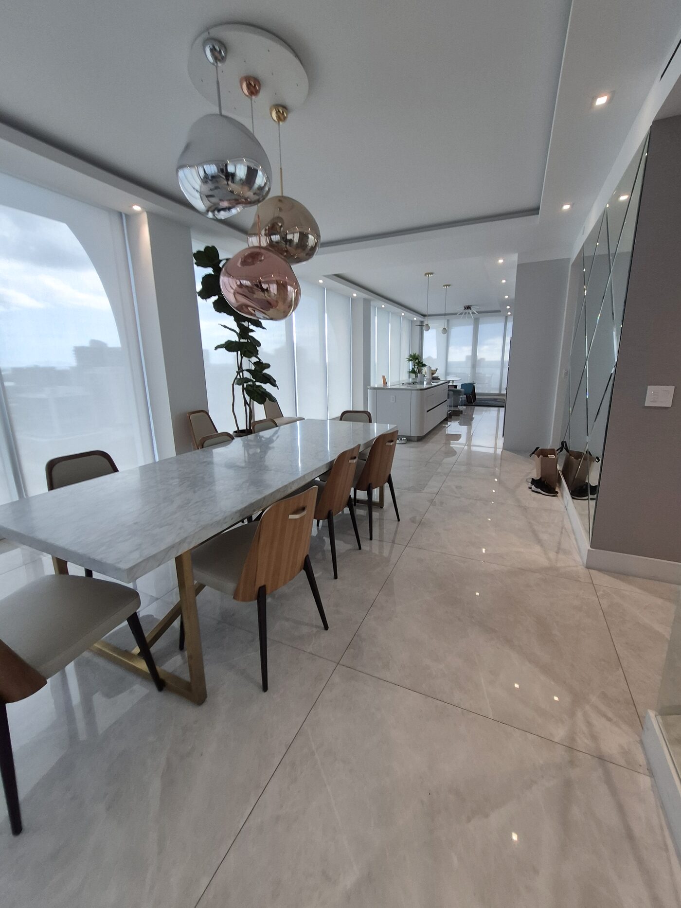 Dining table under the arched corner bay with the kitchen beyond, shades recessed into the ceiling