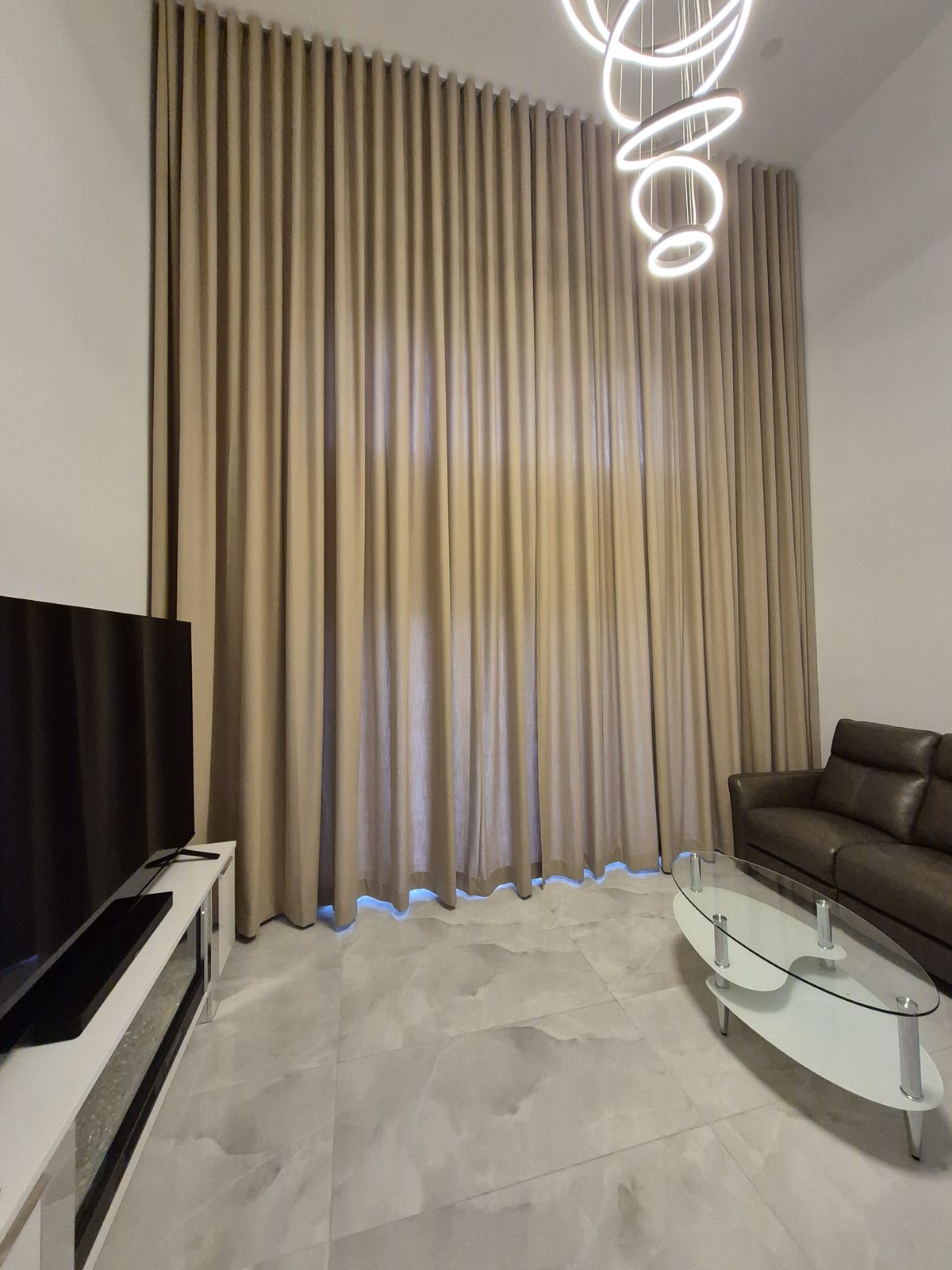 Two-story ripplefold drapery closed across a double-height living room in the evening
