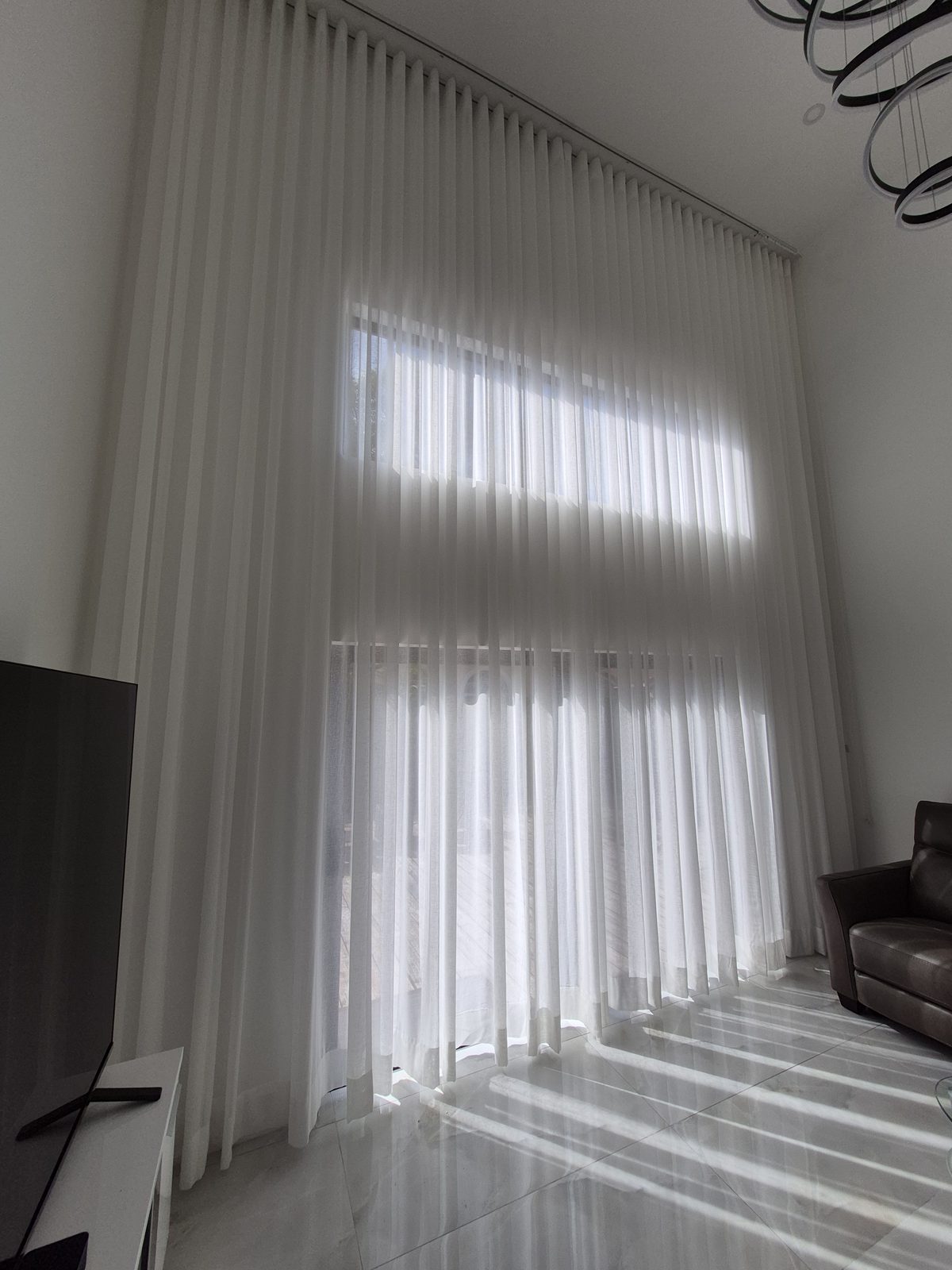 Ripplefold sheer curtains drawn across a two-story wall of glass in the afternoon
